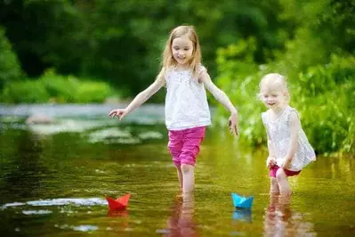 Sisters playing with paper boats in a river