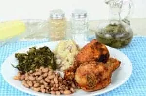 Black eyed peas and turnip greens with deep fried chicken legs and potatoes and spicy vinegar sauce on blue gingham place mat