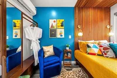 bedroom with wood slat wall, paintings, blue chair and queen bed with colorful decor