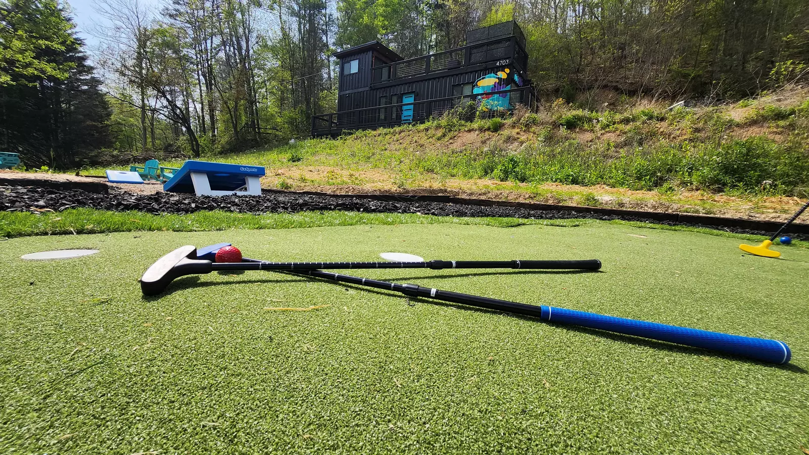 outside view of mini golf clubs, corn hole and background view of black container cabin